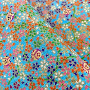 Puede incluir: Una tela de color azul brillante con un patr&oacute;n denso y repetitivo de peque&ntilde;as flores naranjas, blancas, rosas y azul oscuro sobre tallos verdes finos, intercaladas con motivos circulares que contienen dise&ntilde;os geom&eacute;tricos amarillos, morados y blancos.