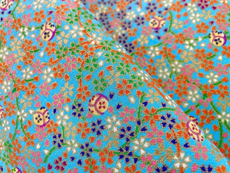 Puede incluir: Una tela de color azul brillante con un patr&oacute;n denso y repetitivo de peque&ntilde;as flores naranjas, blancas, rosas y azul oscuro sobre tallos verdes finos, intercaladas con motivos circulares que contienen dise&ntilde;os geom&eacute;tricos amarillos, morados y blancos.