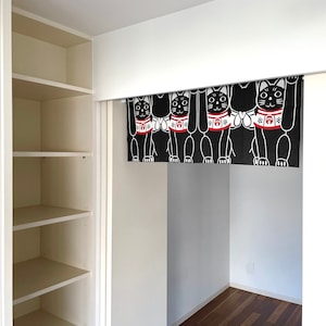 Puede incluir: Cortina japonesa Maneki Neko en blanco y negro en una puerta. La cortina presenta un patr&oacute;n repetido de gatos estilizados con las patas levantadas, con collares rojos. Los gatos est&aacute;n sobre un fondo negro.