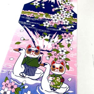 May include: A rectangular fabric panel featuring a graphic print of Mount Fuji in dark blue, surrounded by pink cherry blossoms. Two white swan-shaped floats carry cats wearing green kimonos across a blue and pink gradient water surface.