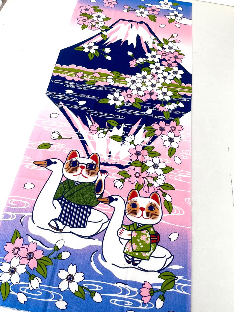 May include: A rectangular fabric panel featuring a graphic print of Mount Fuji in dark blue, surrounded by pink cherry blossoms. Two white swan-shaped floats carry cats wearing green kimonos across a blue and pink gradient water surface.