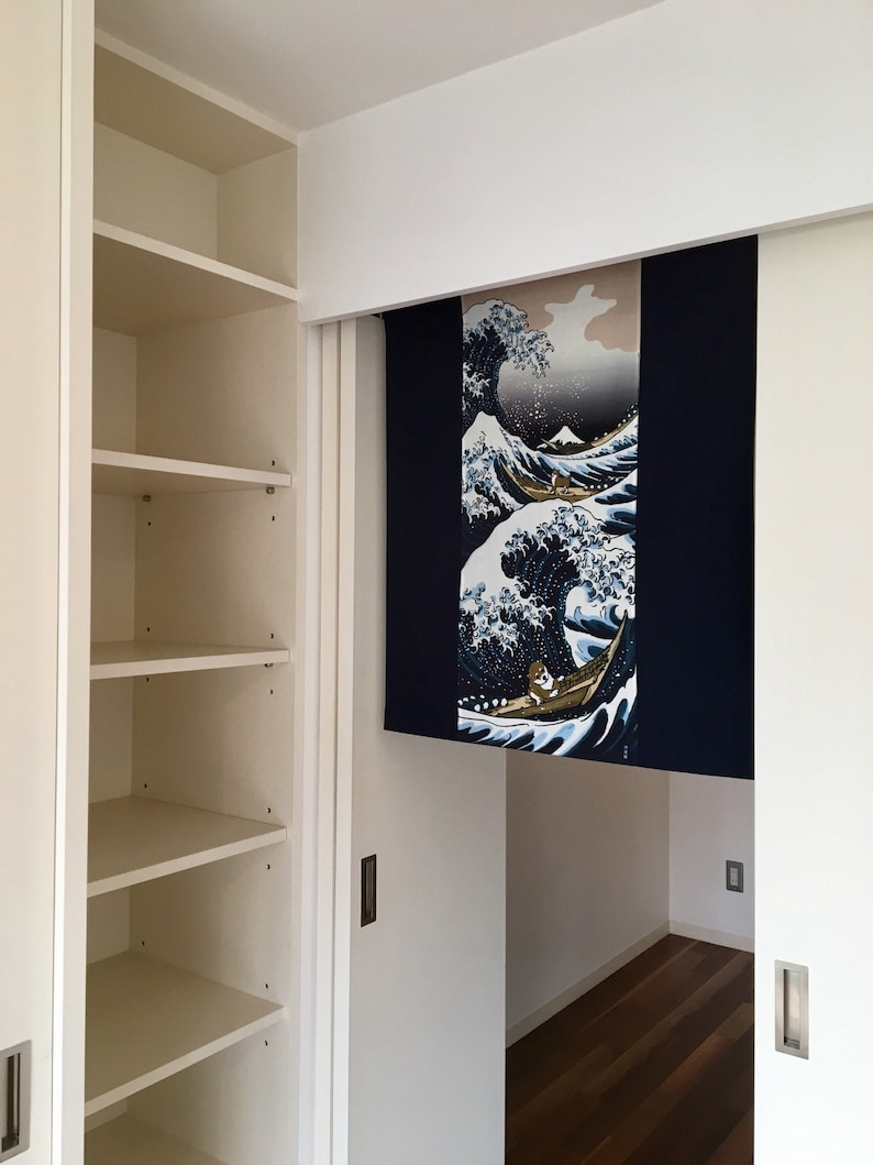 May include: A white closet with shelves and a sliding door. The door is open and reveals a room with a blue and white tapestry hanging on the wall. The tapestry depicts a large wave with a boat and people in it.