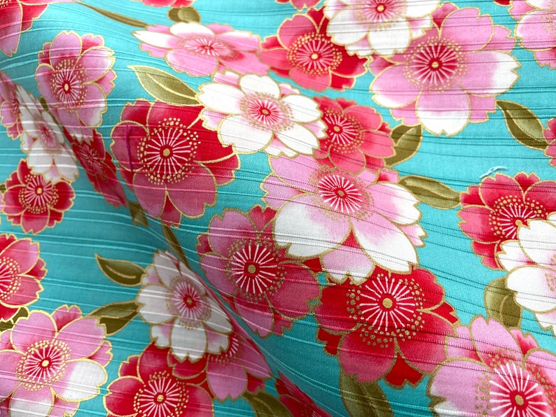 May include: A turquoise fabric with a repeating pattern of pink and red flowers with gold accents. The fabric has a subtle striped texture.