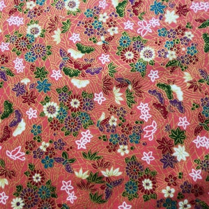 May include: A pink fabric with a repeating pattern of flowers, butterflies, and leaves. The fabric has a gold metallic sheen.