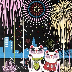May include: Two white lucky cat figurines with black spots and raised paws, wearing colorful scarves and ties, stand in front of a cityscape with fireworks exploding in the night sky.