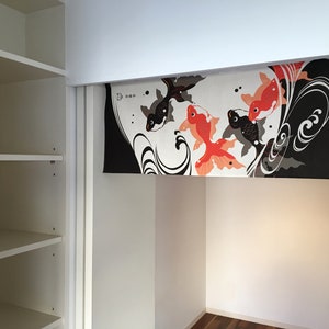 May include: A white closet with a sliding door. The door is open and reveals a black and white fabric panel with a design of red and black fish. The fabric panel is hanging from the top of the closet door.