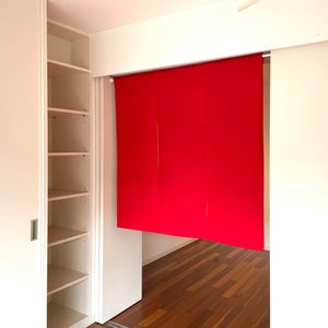 May include: A white closet with sliding doors and shelves. The closet is open and the shelves are empty. There is a red fabric room divider hanging in the doorway.