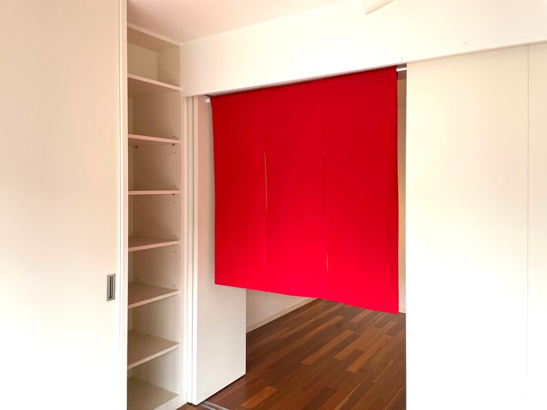 May include: A white closet with sliding doors and shelves. The closet is open and the shelves are empty. There is a red fabric room divider hanging in the doorway.