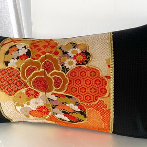 Pode incluir: Travesseiro preto e dourado com um padr&atilde;o floral colorido. O padr&atilde;o apresenta flores vermelhas, laranja, amarelas e brancas, bem como formas geom&eacute;tricas. O travesseiro &eacute; feito de um tecido macio e luxuoso.