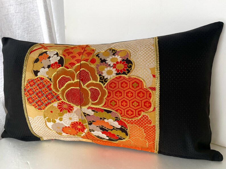 Pode incluir: Travesseiro preto e dourado com um padr&atilde;o floral colorido. O padr&atilde;o apresenta flores vermelhas, laranja, amarelas e brancas, bem como formas geom&eacute;tricas. O travesseiro &eacute; feito de um tecido macio e luxuoso.