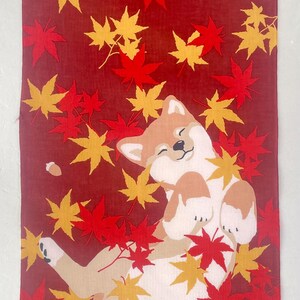 May include: A rectangular fabric wall hanging featuring a tan and white Shiba Inu dog lying on its back amidst a field of red and yellow maple leaves. The design includes a stylized tree stump in the upper corner and small acorns scattered throughout.