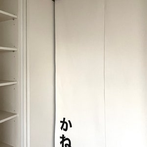 Puede incluir: Puertas correderas de armario blancas con un panel de tela blanca que tiene los caracteres japoneses "か ね" impresos en negro.