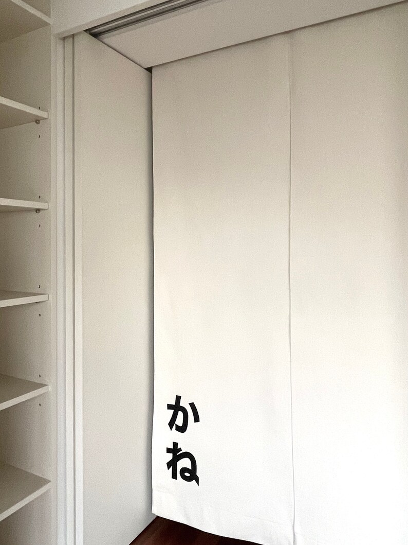 Puede incluir: Puertas correderas de armario blancas con un panel de tela blanca que tiene los caracteres japoneses "か ね" impresos en negro.