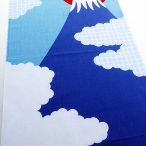 May include: A rectangular fabric runner featuring a graphic print of a dark blue mountain with a white snow-capped peak. The background is a light blue sky with a large red circle representing the sun and several white clouds with a subtle pattern.