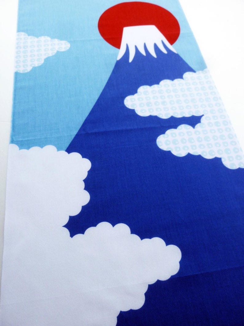 May include: A rectangular fabric runner featuring a graphic print of a dark blue mountain with a white snow-capped peak. The background is a light blue sky with a large red circle representing the sun and several white clouds with a subtle pattern.