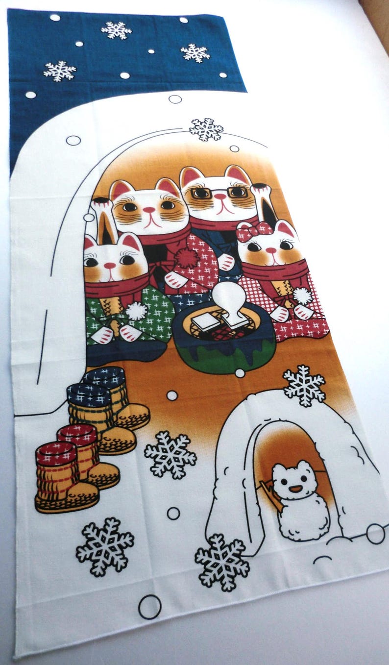 May include: A rectangular fabric wall hanging featuring a winter scene with four illustrated cats wearing scarves and winter clothing, gathered around a small table. A small white dog sits inside an igloo, with snowflakes and boots printed.