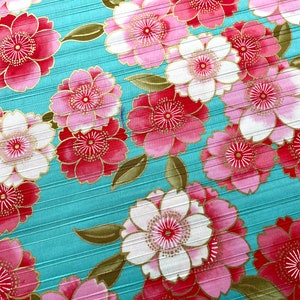 May include: A teal fabric with a repeating pattern of pink and white flowers with gold accents. The flowers have a stylized design with multiple layers of petals.
