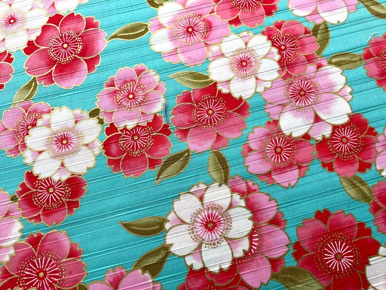 May include: A teal fabric with a repeating pattern of pink and white flowers with gold accents. The flowers have a stylized design with multiple layers of petals.