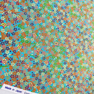 Puede incluir: Una tela azul brillante con un patr&oacute;n denso de peque&ntilde;as flores naranjas, blancas y azul oscuro, enredaderas verdes y motivos circulares. Un borde blanco en la parte inferior muestra el texto Made in Japan Cotton100% y caracteres japoneses.