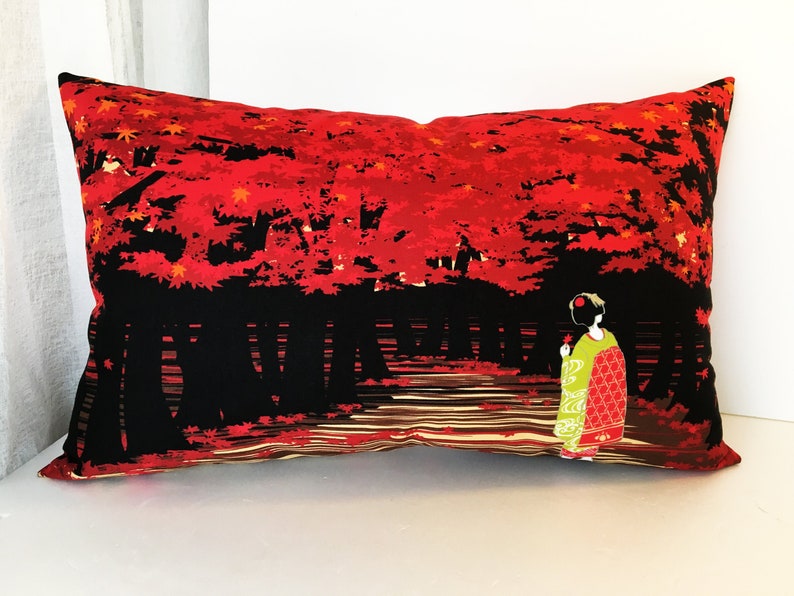 May include: Red and black pillow with a geisha in a green and red kimono walking through a forest of red maple trees.