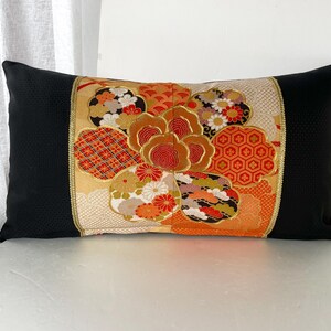 Pode incluir: Uma almofada preta com um padr&atilde;o floral colorido. O padr&atilde;o apresenta uma flor grande com detalhes em vermelho, laranja e dourado. A almofada &eacute; feita de um tecido macio e luxuoso.