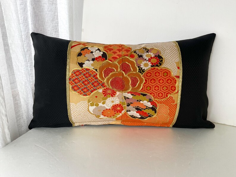 Pode incluir: Uma almofada preta com um padr&atilde;o floral colorido. O padr&atilde;o apresenta uma flor grande com detalhes em vermelho, laranja e dourado. A almofada &eacute; feita de um tecido macio e luxuoso.