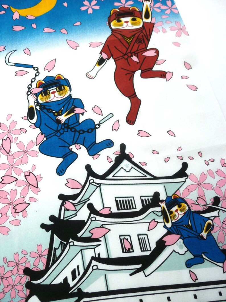 May include: A fabric print featuring three calico cats dressed as ninjas in red and blue uniforms. The cats are depicted jumping and climbing around a white Japanese castle, surrounded by falling pink cherry blossom petals against a blue sky.