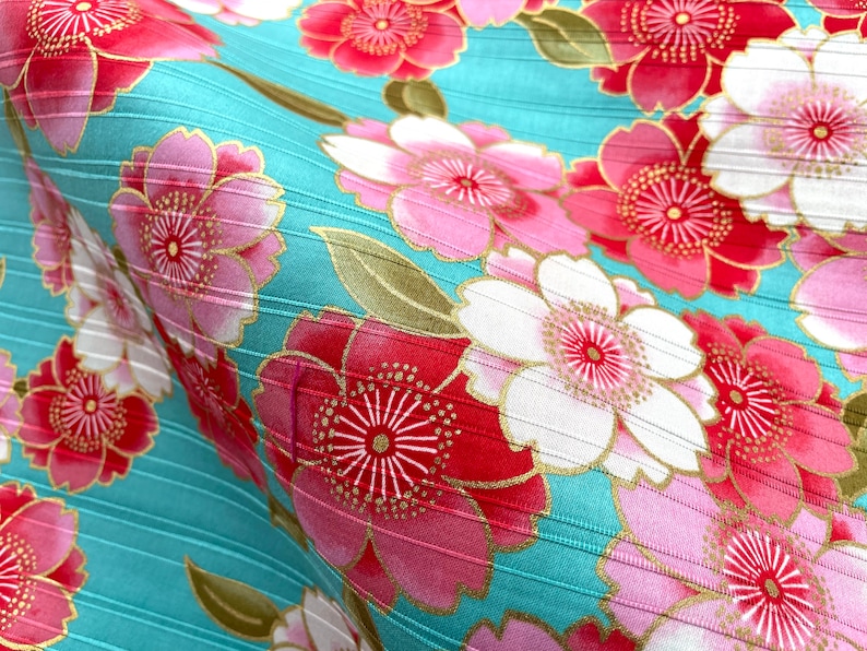 May include: A turquoise fabric with a repeating pattern of pink, red, and white flowers with gold accents. The fabric has a subtle ribbed texture.