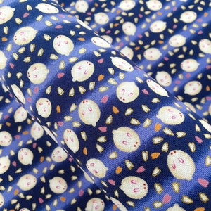 May include: Close-up of a fabric with a repeating pattern of white, cartoon-like rabbits with pink accents and small, scattered leaf shapes. The background is a deep blue with lighter blue stripes.