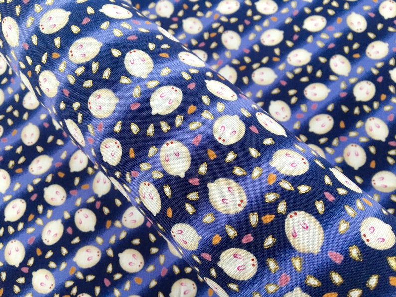 May include: Close-up of a fabric with a repeating pattern of white, cartoon-like rabbits with pink accents and small, scattered leaf shapes. The background is a deep blue with lighter blue stripes.