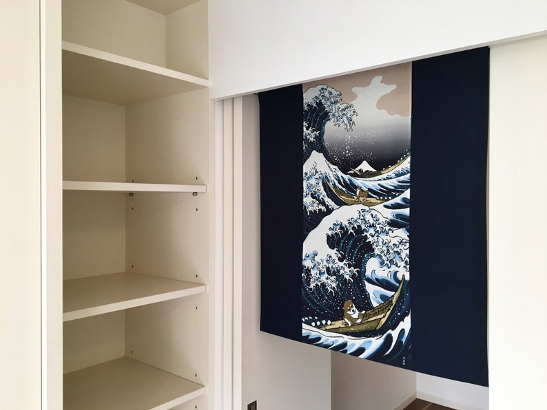 May include: A white bookshelf with four shelves, a white door, and a blue and white tapestry hanging on the wall behind it. The tapestry features a wave design with a boat and a person in it.