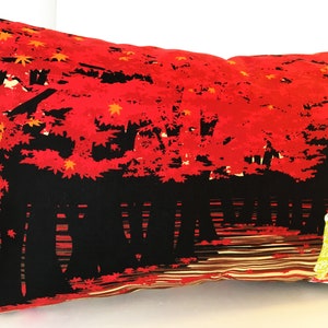 May include: A black and red pillow with a Japanese-inspired design featuring a woman in a yellow and red kimono standing in front of a red maple tree. The background is a black and brown striped pattern.
