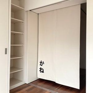 Puede incluir: Una puerta corredera blanca con la palabra japonesa "kana" escrita en negro en la puerta. La puerta est&aacute; abierta para revelar una habitaci&oacute;n con un suelo de madera.