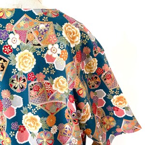Puede incluir: Una camisa de manga corta azul turquesa con un estampado floral colorido. El estampado presenta grandes flores amarillas, flores rosas y formas geom&eacute;tricas.
