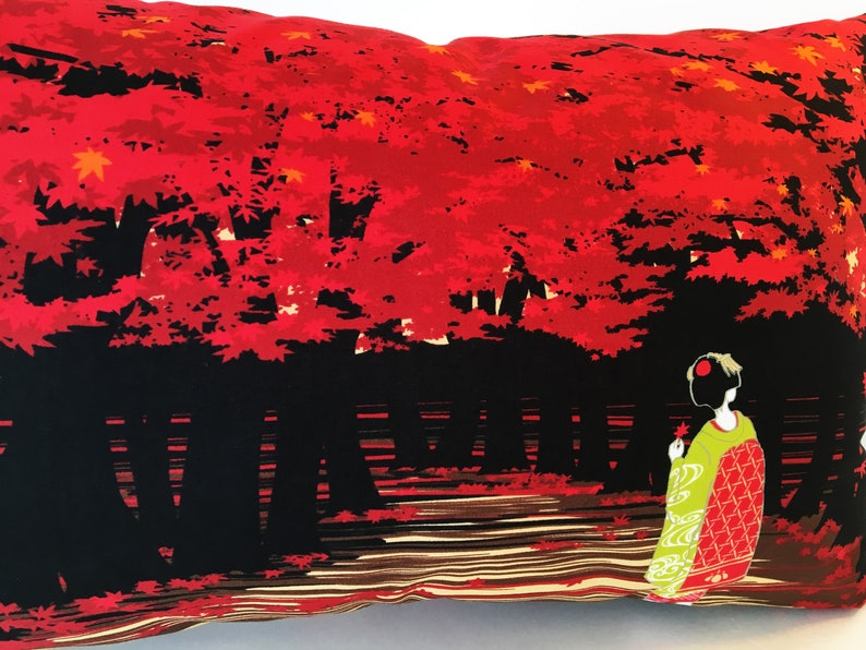 May include: A decorative pillow with a red and black design featuring a Japanese woman in a green and red kimono standing in front of a forest of red maple trees.