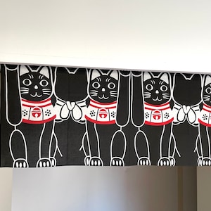 Puede incluir: Cortina Maneki Neko en blanco y negro. La cortina presenta un patr&oacute;n repetido de gatos negros estilizados con patas levantadas, collares rojos y detalles blancos. La cortina est&aacute; colgada en una puerta.