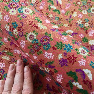 May include: Pink fabric with a repeating pattern of flowers, butterflies, and leaves in shades of red, white, green, blue, and gold.
