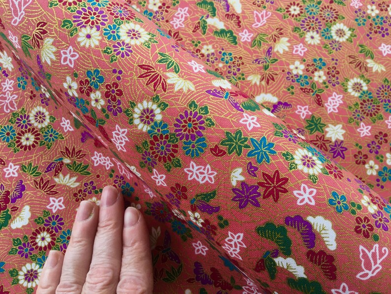 May include: Pink fabric with a repeating pattern of flowers, butterflies, and leaves in shades of red, white, green, blue, and gold.