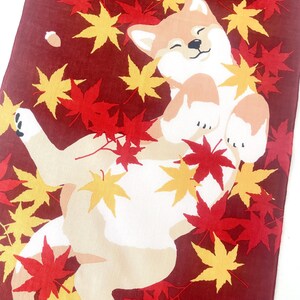 May include: A rectangular textile featuring a tan and white Shiba Inu dog lying on its back amidst a scattering of vibrant red and yellow maple leaves on a deep maroon background. The dog has a joyful expression with closed eyes and paws raised.