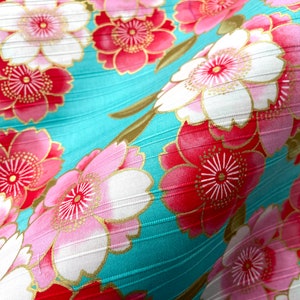 May include: A turquoise fabric with a repeating pattern of pink and red flowers with gold accents. The fabric has a subtle ribbed texture.