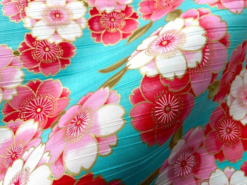 May include: A turquoise fabric with a repeating pattern of pink and red flowers with gold accents. The fabric has a subtle ribbed texture.