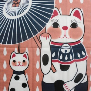 May include: A pink fabric panel with a white cat holding a blue and white umbrella. The cat is wearing a blue and red bib with white spots. The background is a pink fabric with white raindrops.