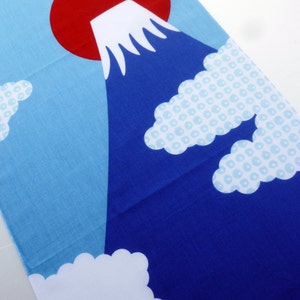 May include: A rectangular fabric textile featuring a graphic illustration of a dark blue mountain with a white snow-capped peak. A large solid red circle sits behind the mountain against a light blue sky, accented by white and light blue patterned clouds.