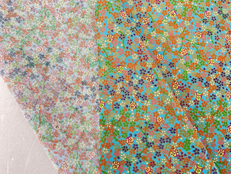 Puede incluir: Una tela con un patr&oacute;n denso de peque&ntilde;as flores de cerezo y motivos circulares en tonos naranja, verde, azul y dorado. El dise&ntilde;o se presenta sobre un fondo turquesa brillante, con una secci&oacute;n doblada que muestra una versi&oacute;n m&aacute;s clara.