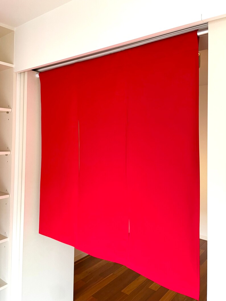 May include: Three red fabric panels hanging from a track system, creating a room divider. The panels are made of a smooth, solid fabric.