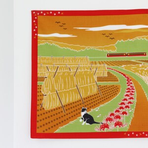 May include: A colorful illustration of a rural Japanese landscape with a cat, hay bales, a train, and red spider lilies. The scene is set against a sunset sky with a few birds flying overhead.