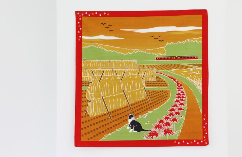 May include: A colorful illustration of a rural Japanese landscape with a cat, hay bales, a train, and red spider lilies. The scene is set against a sunset sky with a few birds flying overhead.