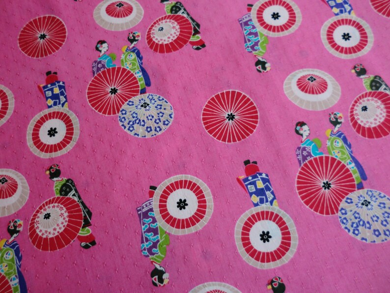 May include: Pink fabric with a repeating pattern of geishas, umbrellas, and flowers. The umbrellas are red, white, and black. The geishas are wearing traditional Japanese clothing.