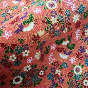 May include: A pink fabric with a repeating pattern of butterflies, flowers, and leaves. The fabric has a gold metallic sheen.