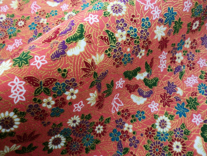 May include: A pink fabric with a repeating pattern of butterflies, flowers, and leaves. The fabric has a gold metallic sheen.